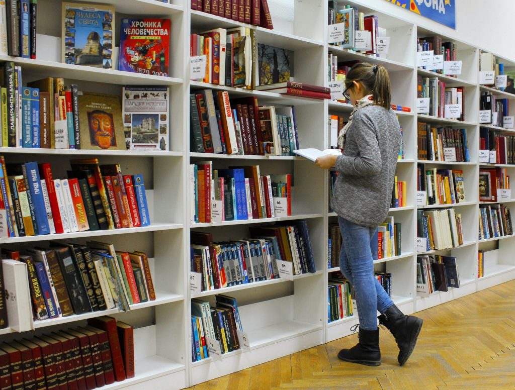 A young woman stands reading a book in a well-stocked library.