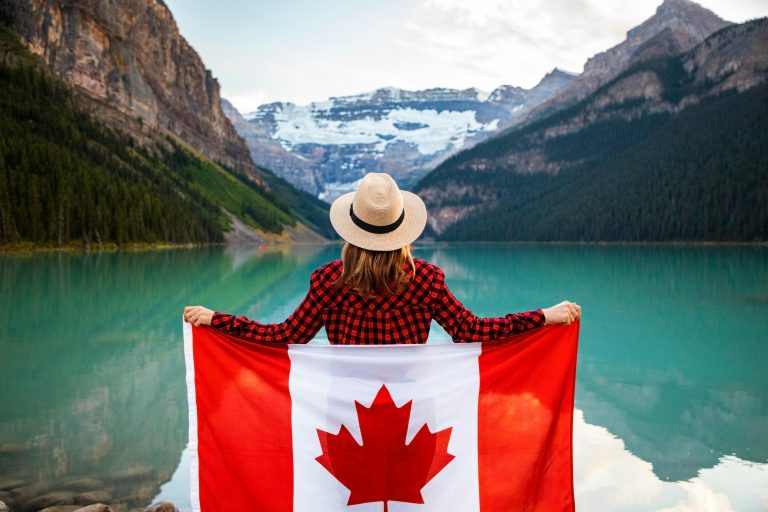 Woman holding a Canadian flag at stunning Lake Louise, Alberta, embracing nature and patriotism.