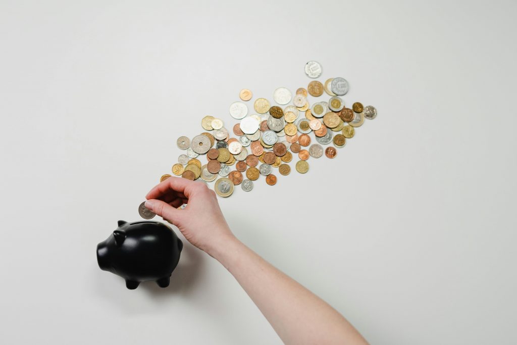 Person placing coin into a black piggy bank with scattered coins, symbolizing savings and finance.