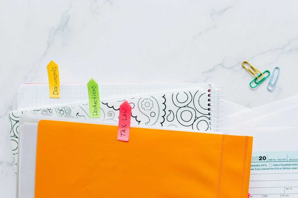 Top view of tax documents organized with colorful sticky notes on a marble desk.