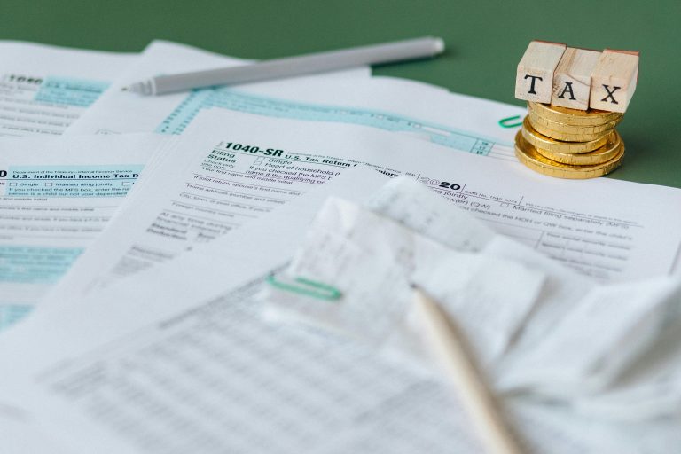 Stack of tax forms and coins with a 'TAX' stamp, symbolizing finance and accounting.