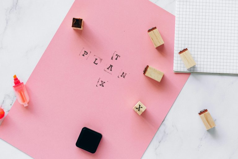 Flat lay of a creative planning setup featuring alphabet stamps, pink paper, and markers for artistic ideas.