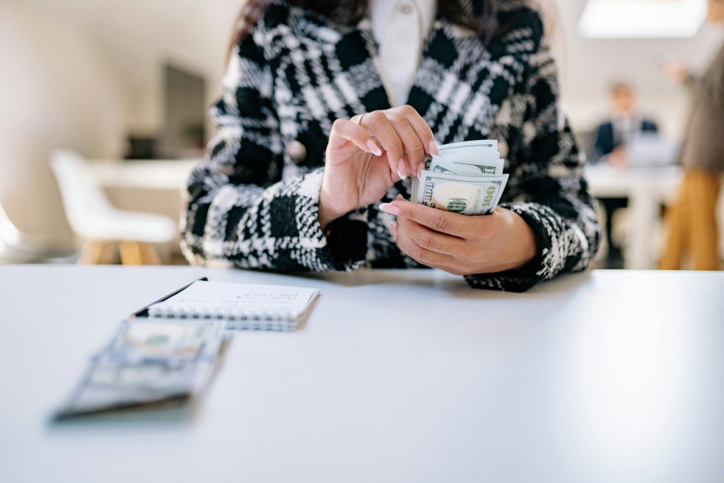 A close-up of a woman counting US dollars in an office environment, symbolizing financial management.