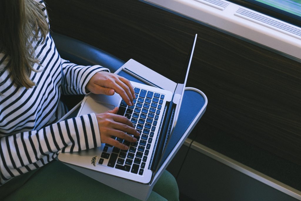 A woman in a striped shirt types on a laptop while traveling on a train, showcasing remote work lifestyle.