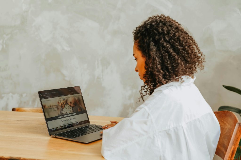 A woman in a white shirt with curly hair researching online using her laptop.