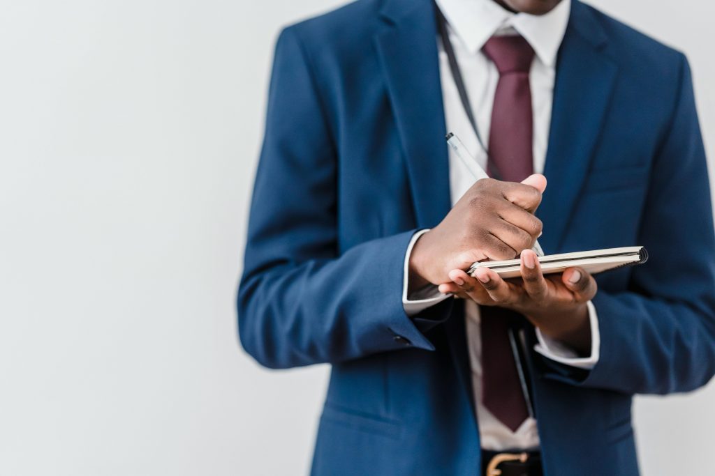 Close-up of a professional writing notes in a notebook wearing a blue suit and red tie.