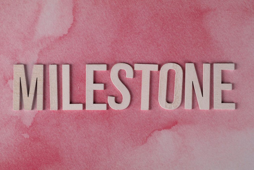 Wooden MILESTONE text on a pink watercolor background, perfect for celebrations or achievements.