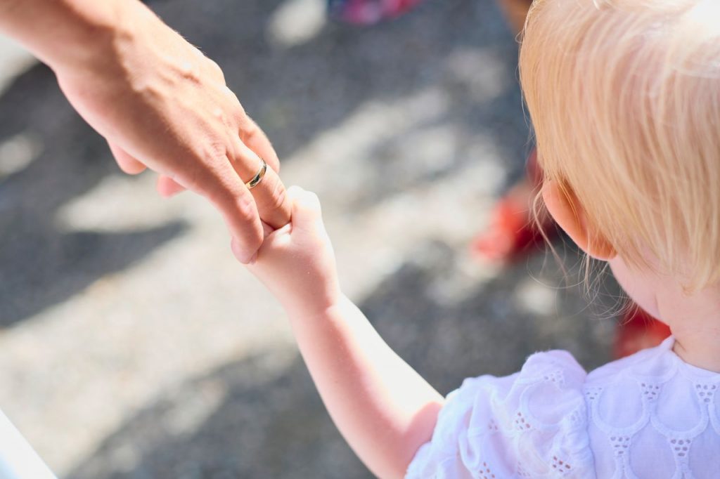 Blonde child holding parent's hand outdoors, symbolizing love and protection.
